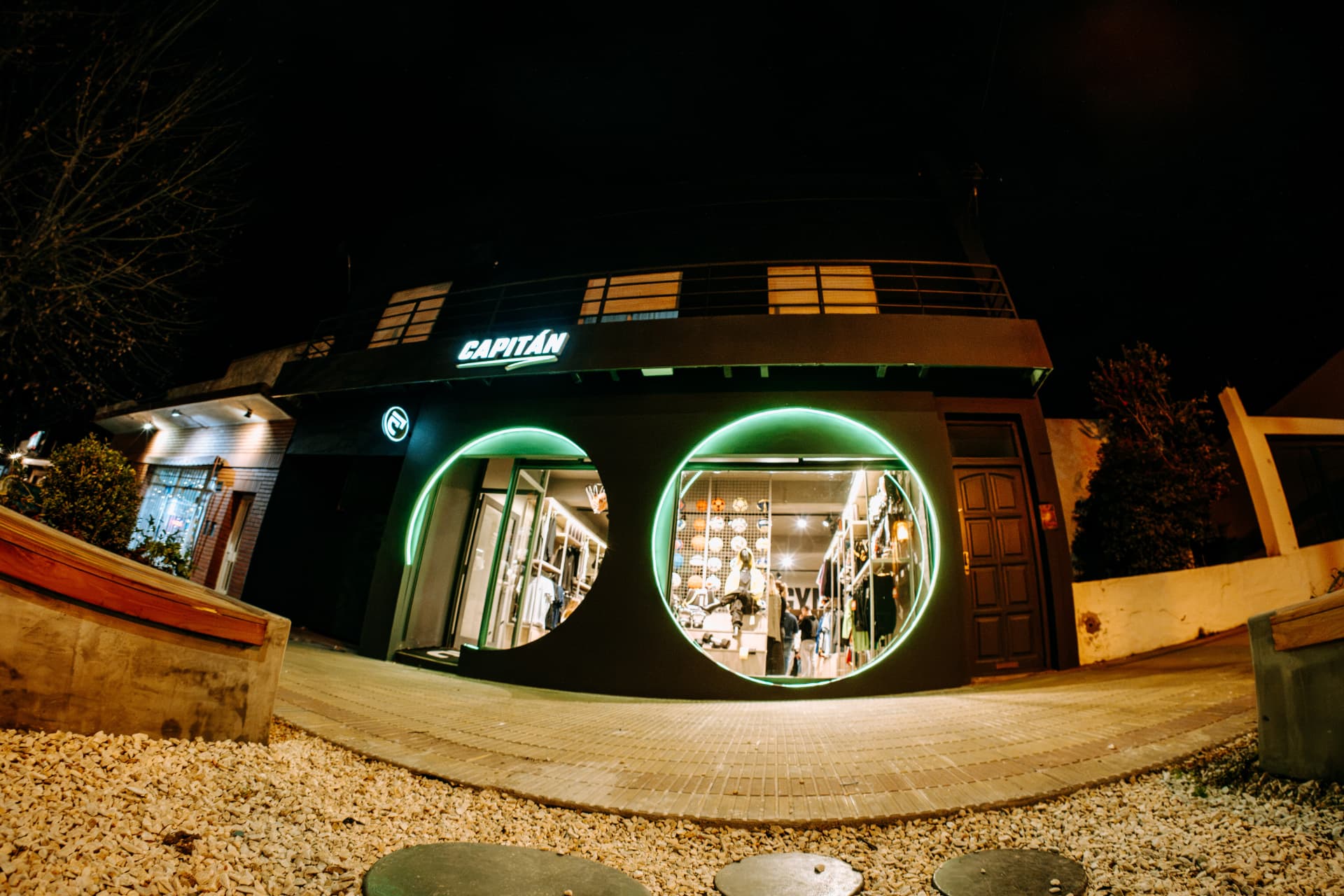 Fachada nocturna del local de Capitán Deportes en Tandil, con sus vidrieras circulares iluminadas